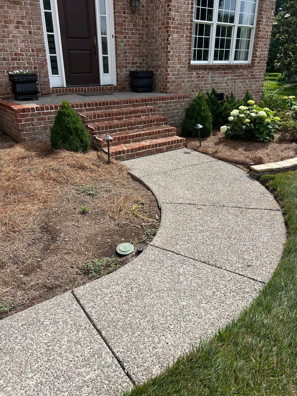 Curved concrete walkway leading to a brick home with steps and landscaping features.