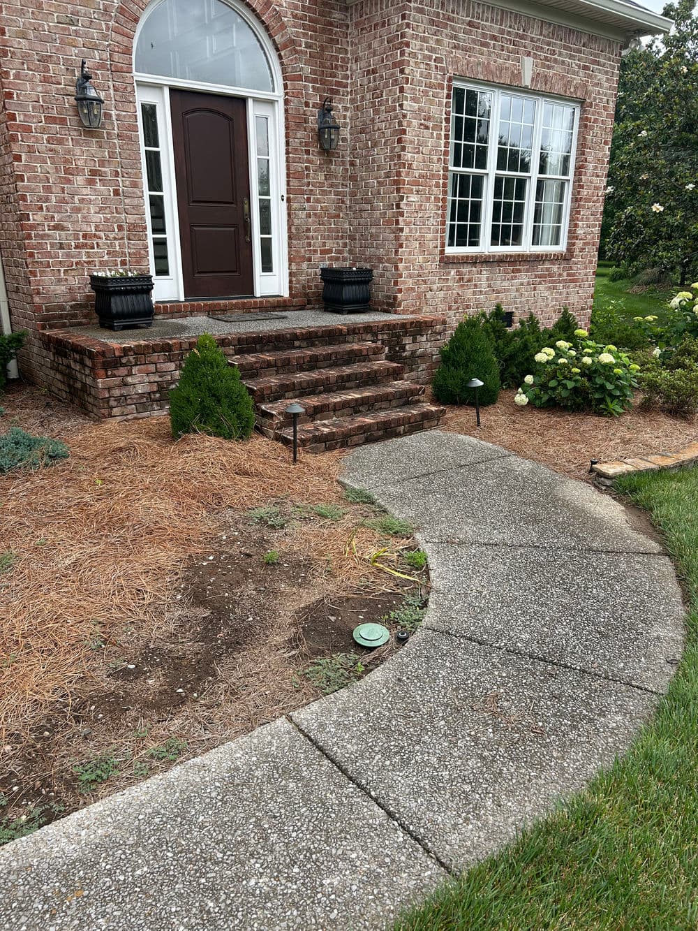Front entrance of a brick house with stairs, planters, and a curved concrete walkway.